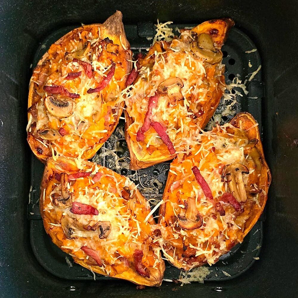 Patates douces farcies aux lardons et champignons, gratinées au fromage râpé, dans le panier de l'Airfryer à la sortie de la cuisson.