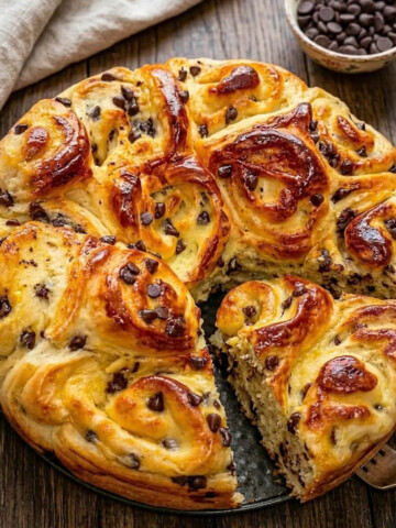 Brioche moelleuse aux pépites de chocolat faite maison, vue de dessus sur un fond rustique avec un bol de pépites de chocolat.