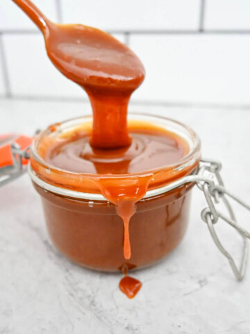 Une cuillère en métal soulève une généreuse dose de sauce caramel au beurre salé onctueuse au-dessus d'un bocal en verre.