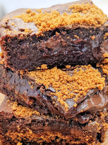 Trois parts de fondant au chocolat ultra fondant empilées sur une planche en bois, parsemées de brisures croustillantes de biscuits spéculoos. Le cœur du gâteau est coulant et brillant.