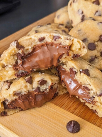 Gros plan de cookies moelleux fourrés au Nutella sur une planche en bois, avec un cœur fondant à la pâte à tartiner.