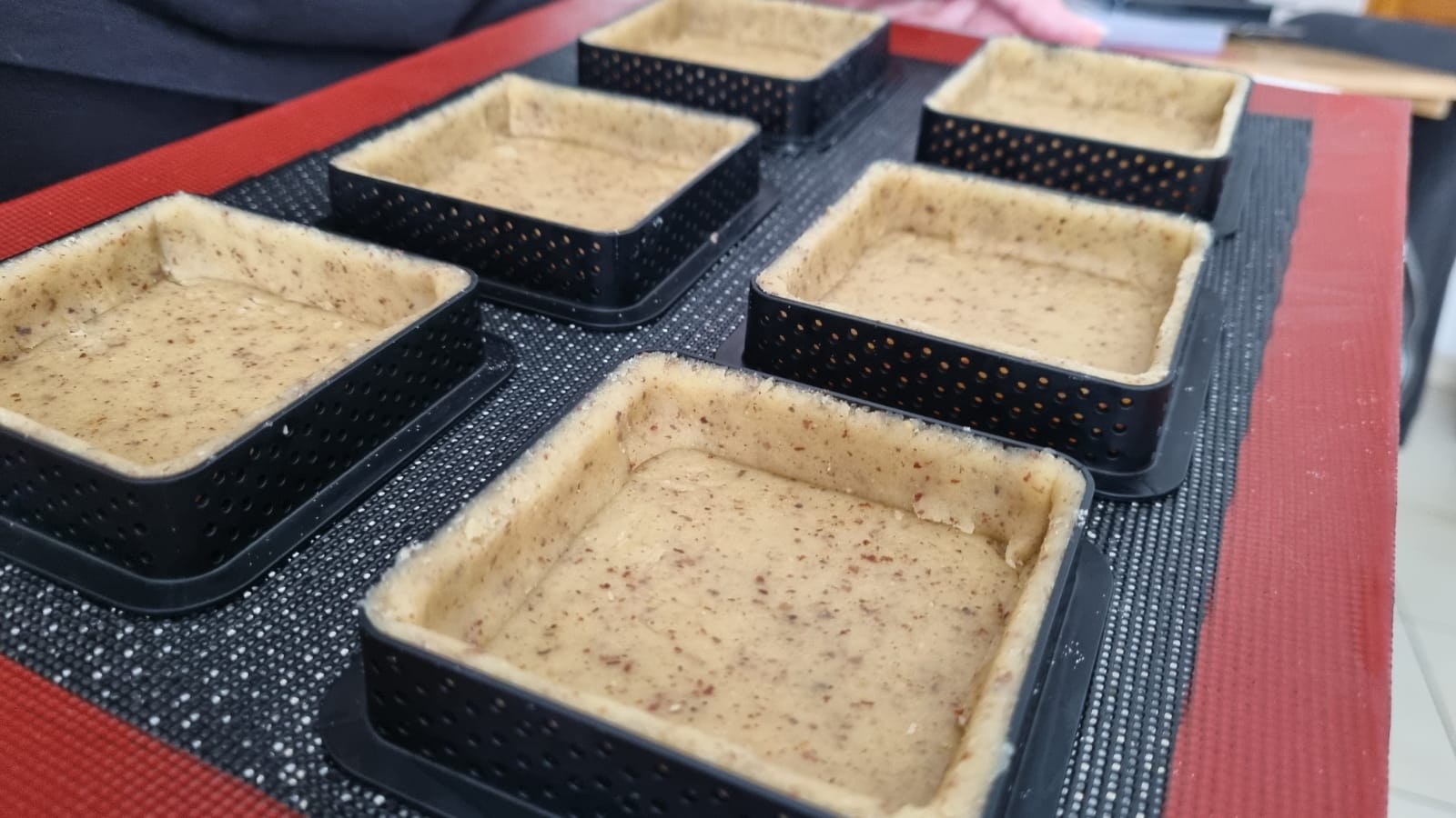Pâte sablée dans des moules a tartelettes sur une feuille de cuisson en silicone