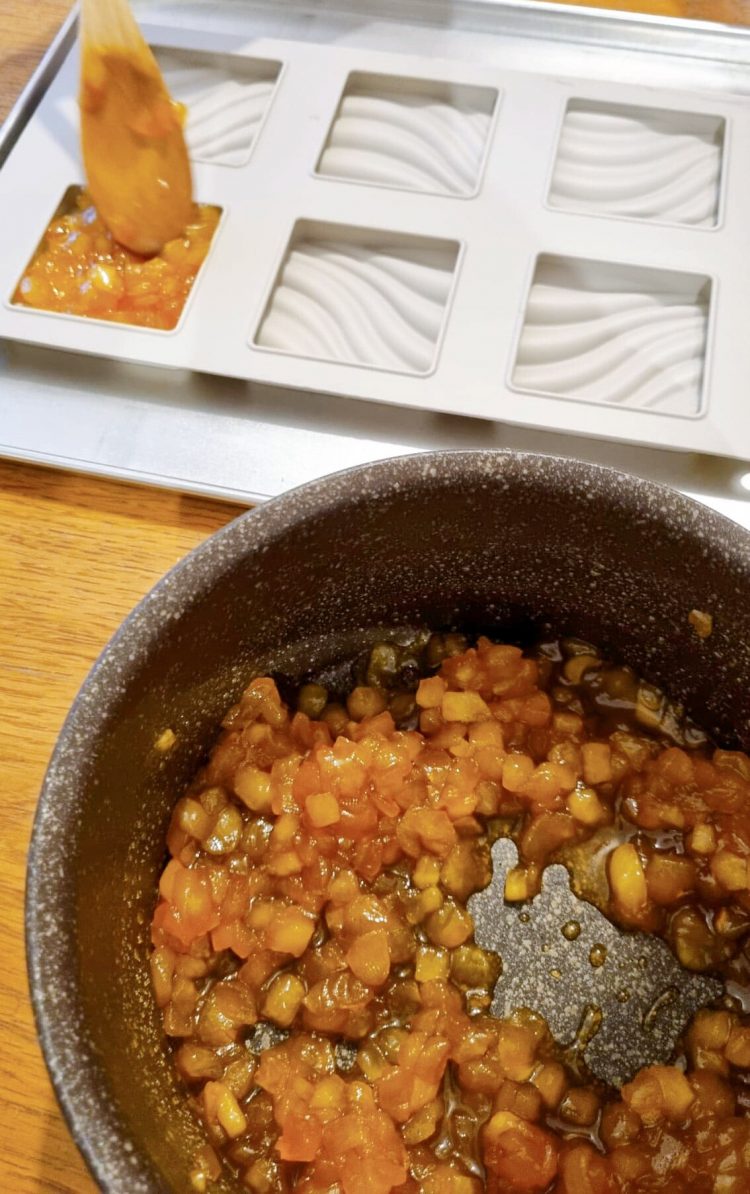 Une casserole avec des pommes caramélisées et un moule en silicone pour faire des tartelettes tatin aux pommes.