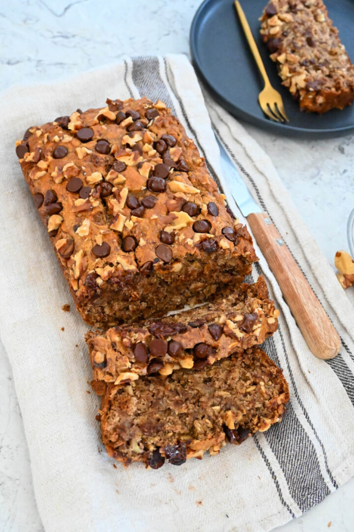 Banana bread découpé en tranches sur un torchon beige avec un couteau sur le coté.