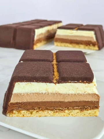 Tranche d'entremets aux trois chocolats avec des couches distinctes de mousse chocolat noir, lait et blanc sur une base de biscuit Joconde moelleux.