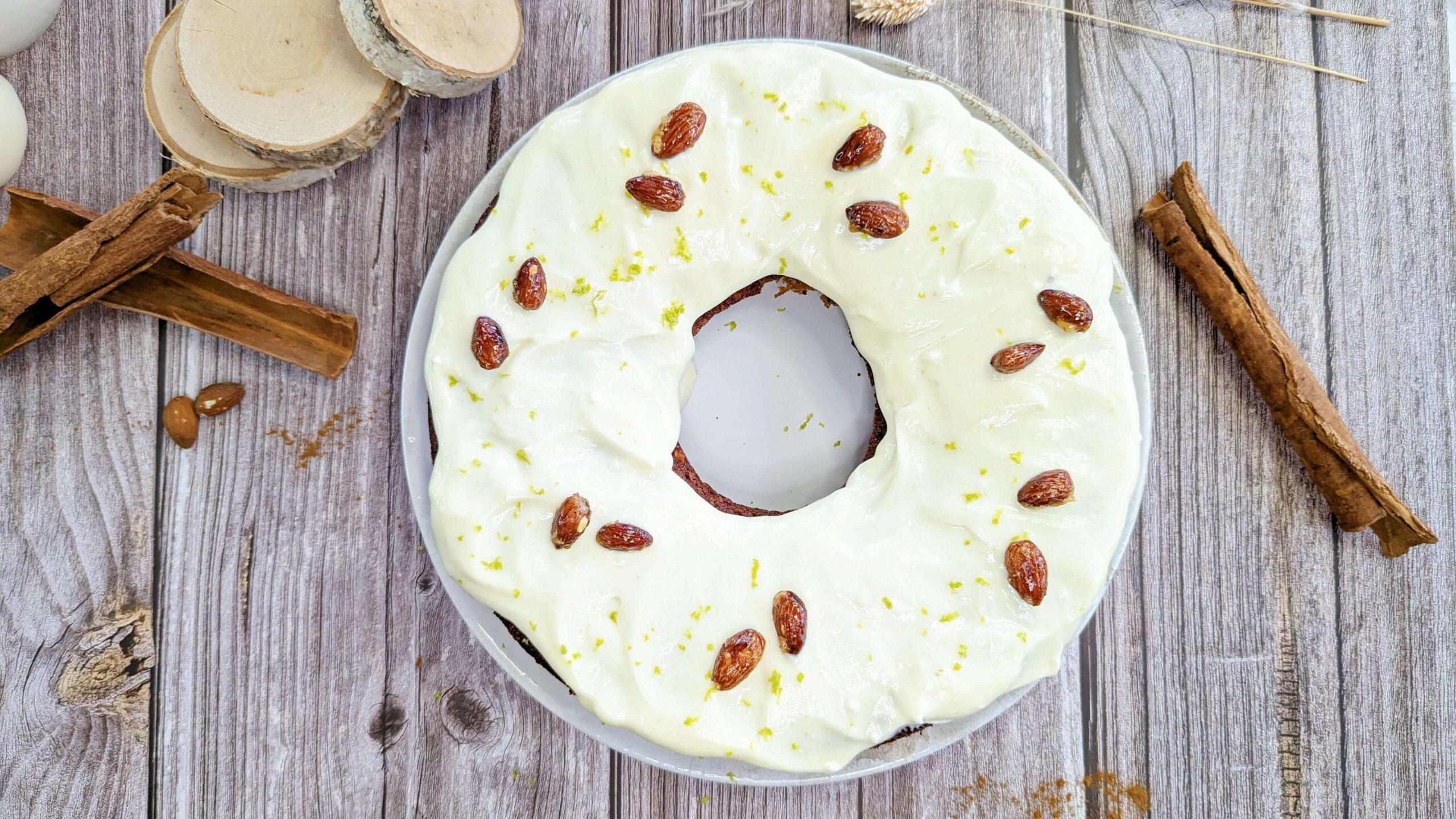 Un carrot cake vu d'en haut sur une assiette avec bâtons de cannelle, sur un fond de couleur bois.