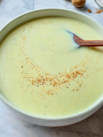Un bol contenant de la sauce béchamel fait maison, sur fond marbré blanc, noix de muscade.