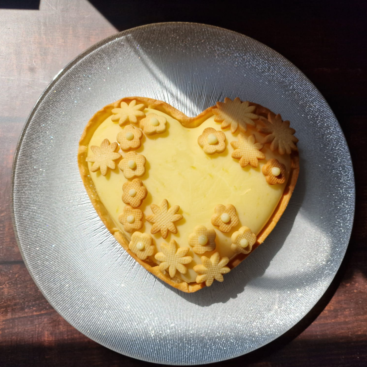 Tarte au citron en forme de coeur dans une assiette gris clair métallique.