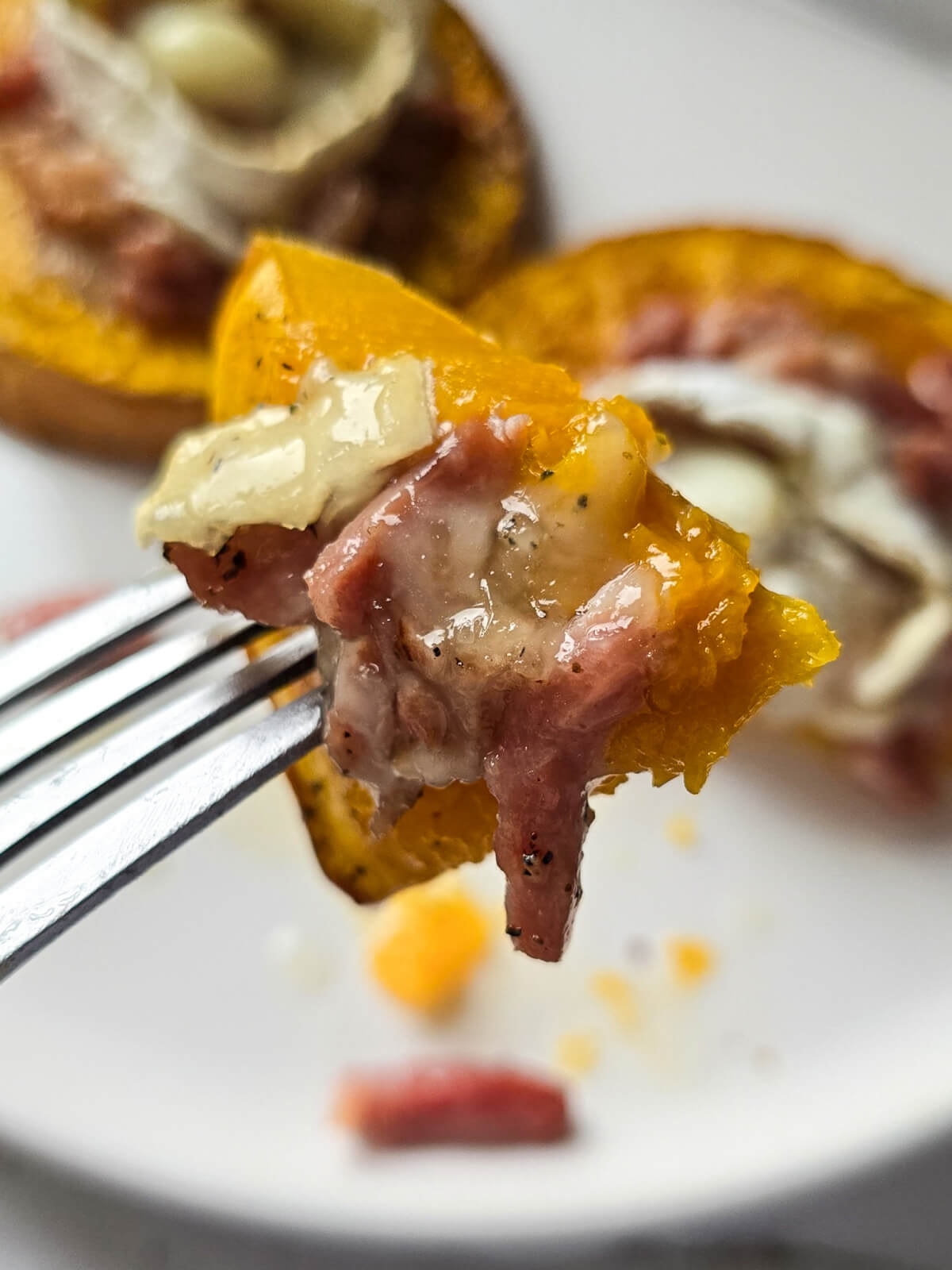 Gros plan sur un morceau de rondelle de butternut rôti au four avec du chèvre et lardons sur une fourchette.
