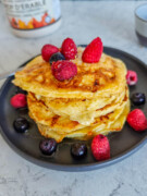 Des pancakes protéinés dans une assiette noire avec des fruits rouges, sur un fond blanc marbré.