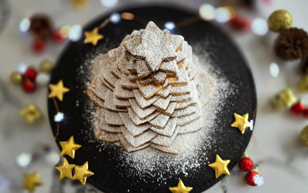 Des biscuits en forme d'étoile recouvert de sucre glace et empilés les uns sur les autres dans une assiette noire, et des décorations de Noel.