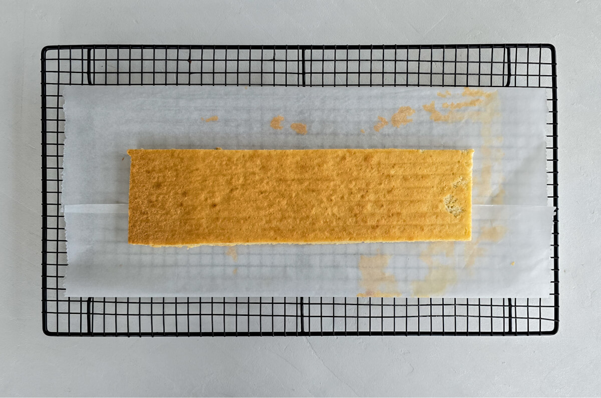 Biscuit joconde découpé pour Bûche de Noël poire caramel sur une plaque de refroidissement avec papier sulfurisé.