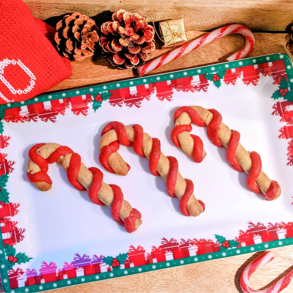 Sablés de Noel en forme de sucre d'orge (rouge et blanc0 sur une assiette décorative de Noel sur un fond en bois.