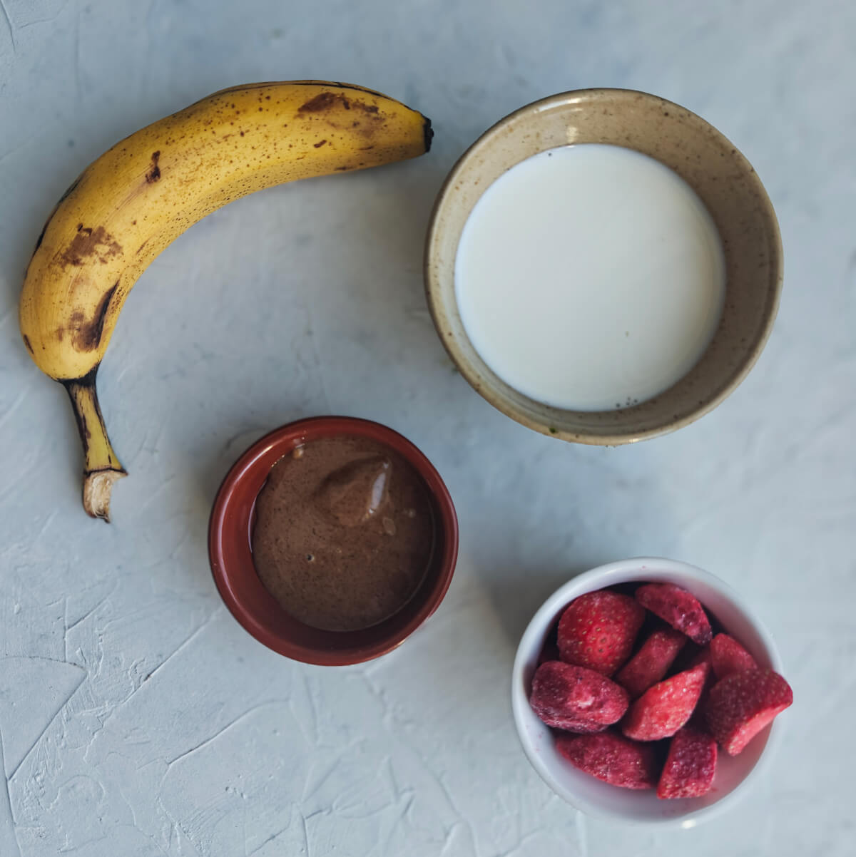 Des ingrédients pour faire un smoothie fraise banane sur un fond blanc.