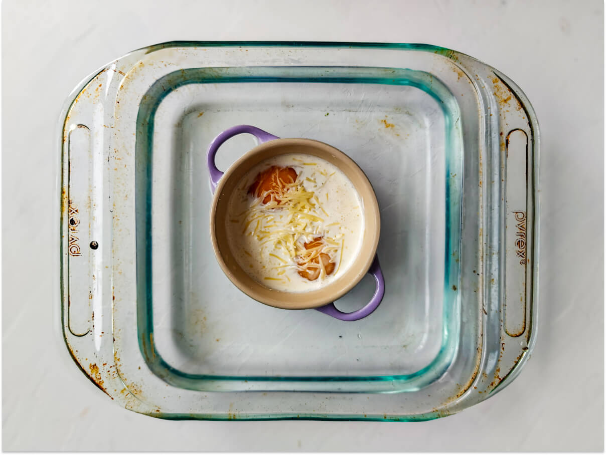 Des oeufs dans une cocotte individuelle dans un plat Pyrex transparent, sur un fond blanc.