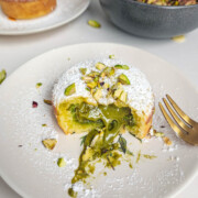 Un moelleux aux pistaches ouvert avec un coeur coulant a la pistache, sur une assiette, fourchette sur le coté.