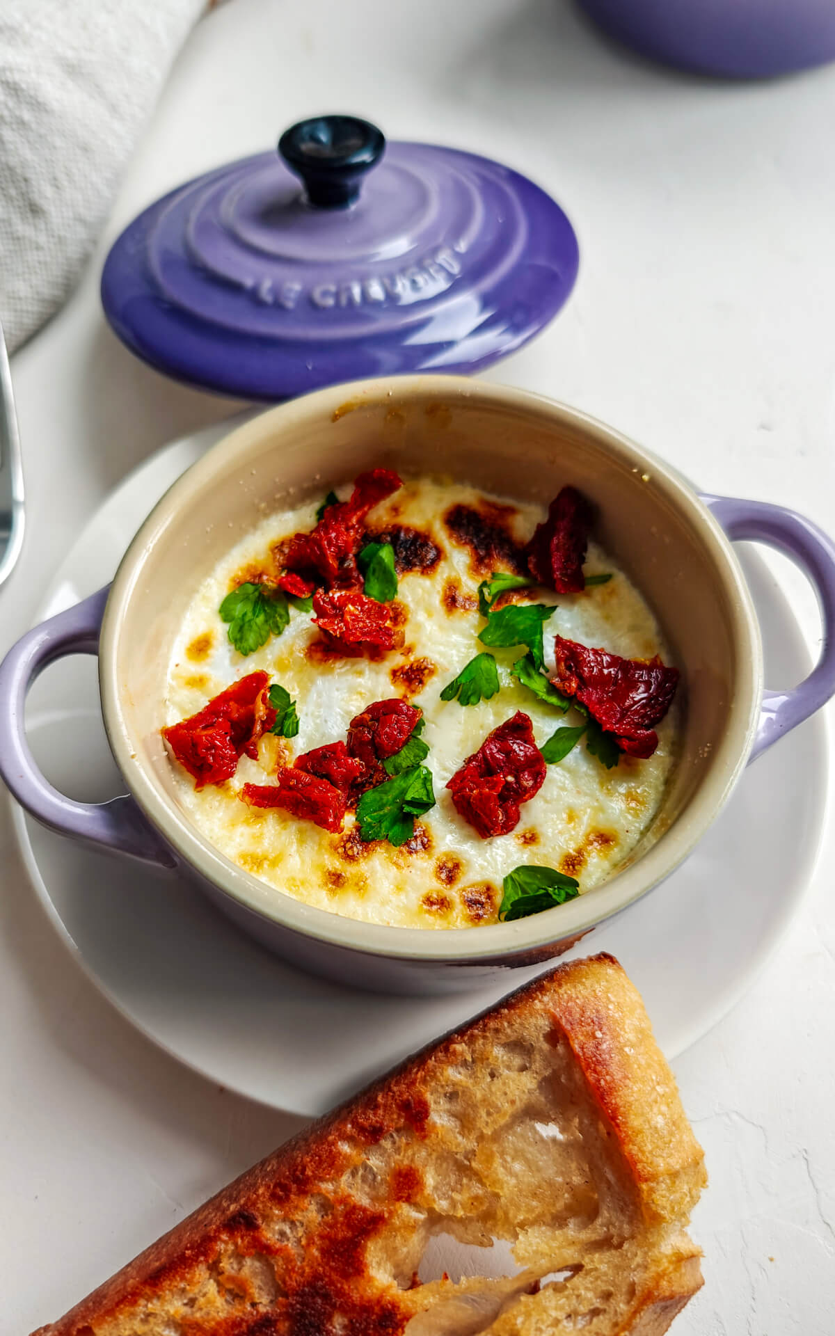 Des oeufs dans une mini cocotte avec du pain grillé, sur un fond blanc. Torchon sur le coté.