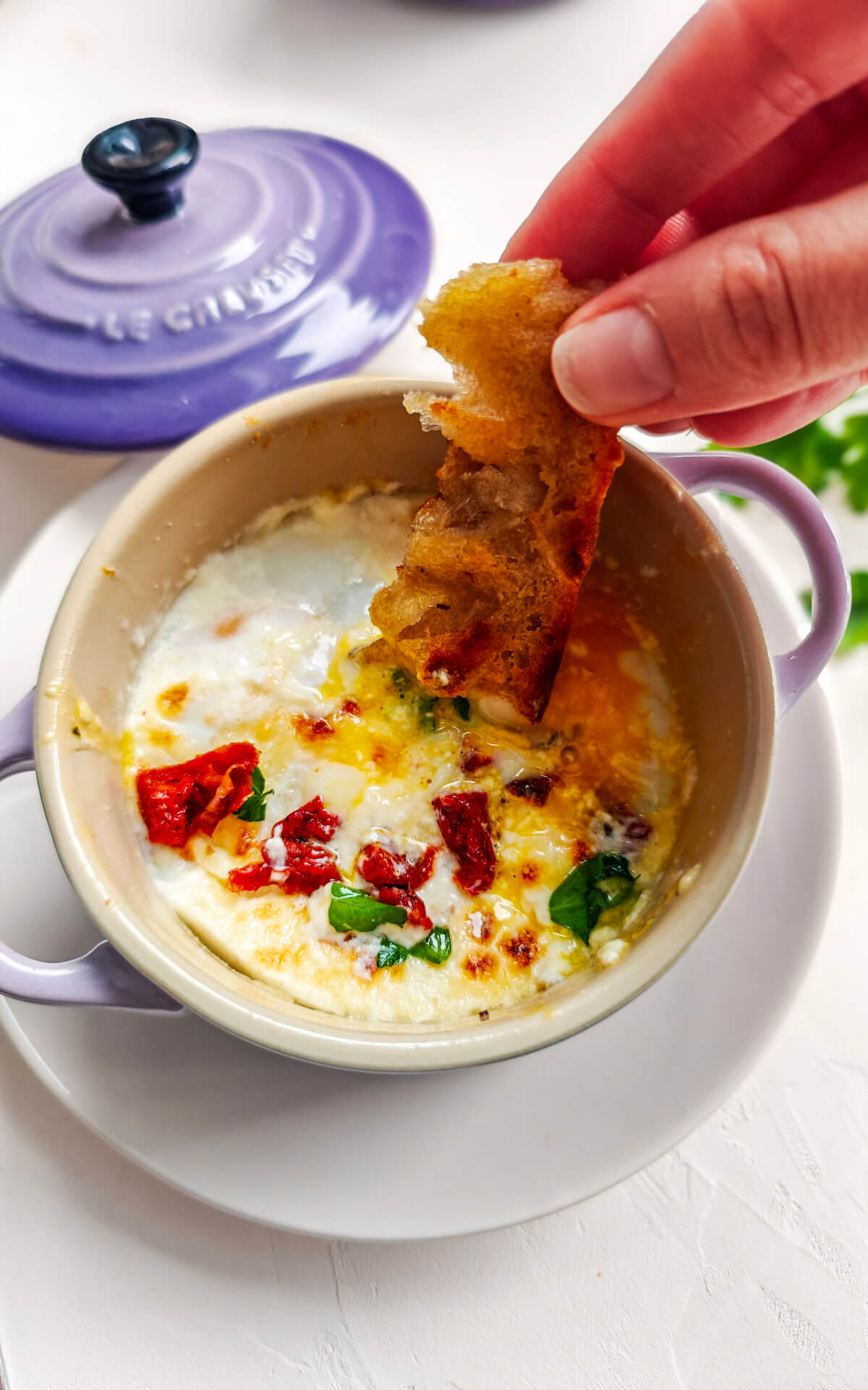 Des oeufs dans une cocotte indviduelle avec une main trempant un bout de pain.