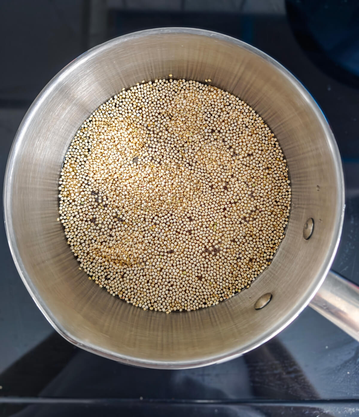 Du quinoa non-cuit dans une casserole sur une cuisinière noire.