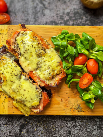 Des aubergines façon pizza sur une planche de bois, laitue et tomates cerises sur le coté.