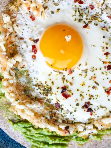 Un oeuf feta sur une tortilla avec un avocat, sur une assiette bleue.