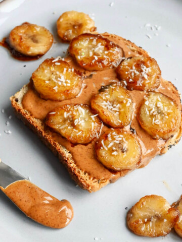 Une tartine beurre d'amande banane caramélisée sur une assiette blanche, couteau à beurre sur le côté.