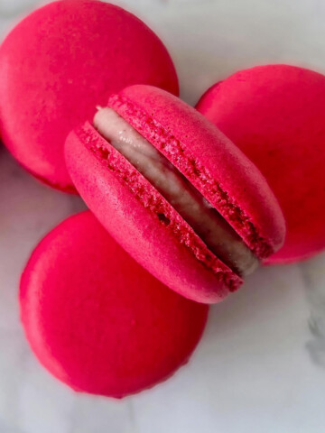 Des macarons à la framboise, ganache fondante sur un fond de couleur blanc marbré.