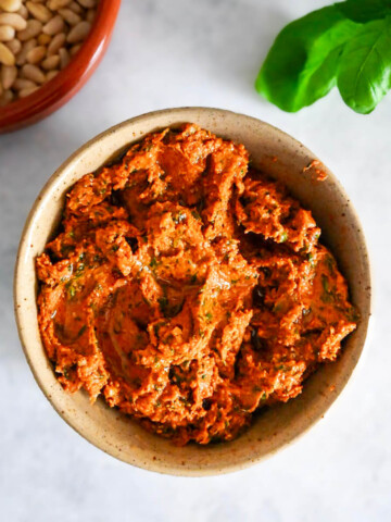 Du pesto rosso dans un bol, basilc et pignons sur le coté.