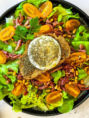Une salade de chèvre chaud et lardons dans une assiette creuse noire.