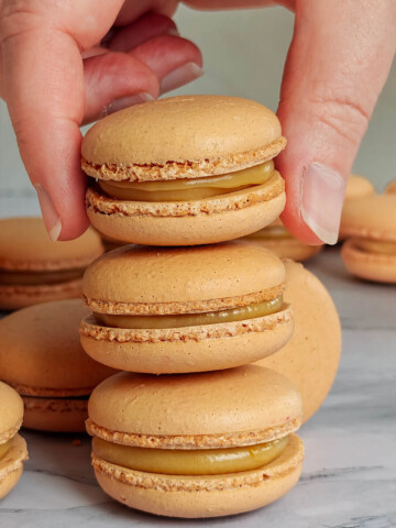 Une main tenant un macaron caramel beurre salé, sur un deux autres macarons.