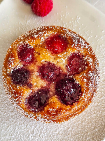 Une tartelette framboise coupé en deux, sur une assiette blanche, framboise en deuxième plan.