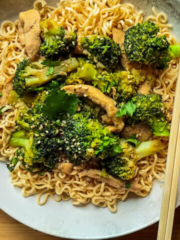 Des nouilles sautées au poulet avec des baguettes chinoises, dans une assiette creuse blanche.