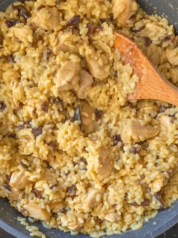 Du risotto poulet champignons dans une poêle, cuillère en bois sur le côté.