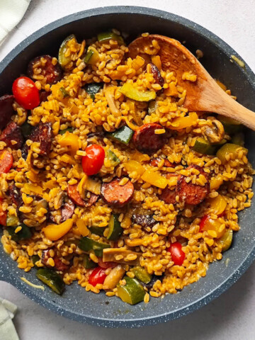 Une poêle contenant des ingrédients avec une cuillère en bois, pour une recette de one pot blé chorizo.