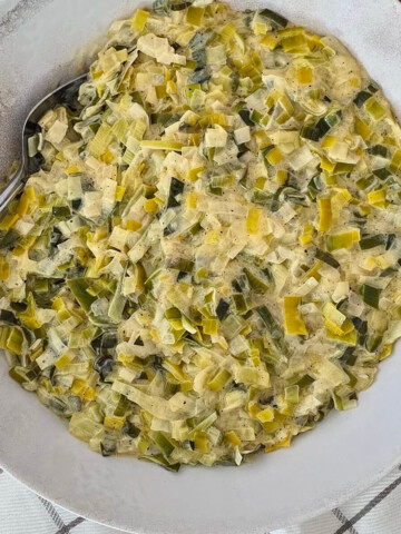 Une fondue de poireaux dans un plat de présentation blanc, avec un torchon.