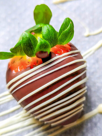 Une fraise enrobée de chocolat au lait avec un filet de chocolat blanc.