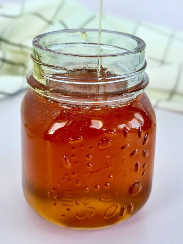 Filet de caramel liquide maison coulant d'une cuillère en bois dans un bocal en verre.