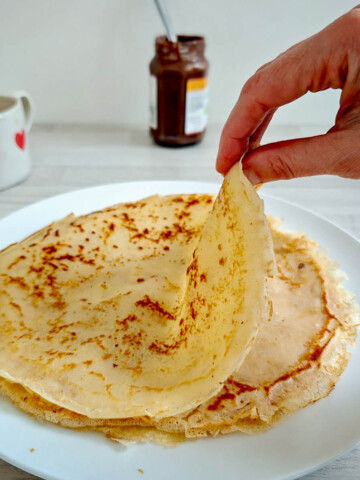 Des crêpes sans gluten dans une assiette blanche, café et pâte à tartiner sur le côté.