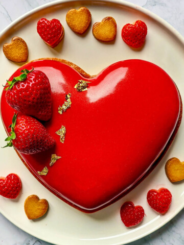 Un entremets fraise avec un glaçage miroir transparent sur une assiette blanche.