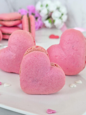 Des macarons en forme de cœur présentés dans une assiette blanche, idéaux pour la Saint-Valentin ou la Fête des Mères.