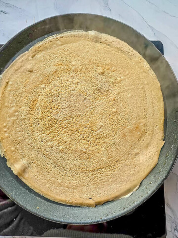 une galette de sarrasin fine et fumante sur une poêle chaude pour montrer la souplesse de la pâte maison.