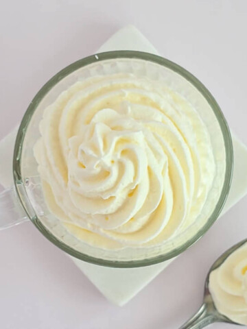 Vue de dessus d'une tasse transparente contenant une rosace de crème chantilly blanche aérienne, mettant en avant la précision du pochage à la douille.