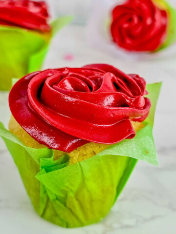 Des cupcakes vanille avec une crème au beurre rouge vif, présentés sur un fond marbrée blanc.