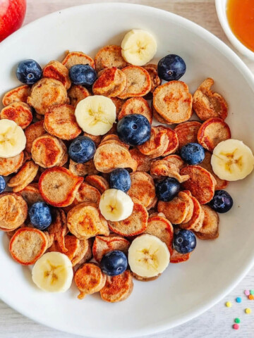 Des mini pancakes banane moelleux, dans une assiette avec des fruits.