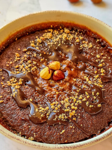 Alt text : Bowl cake au chocolat et noisettes parsemé d'éclats de noisettes et d'un coulis de chocolat fondant, servi dans un bol beige sur un plan de travail en marbre.
