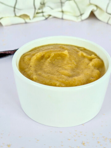 Une compote de pommes vanille dans un ramequin blanc, torchon et gousse vanille sur le côté.