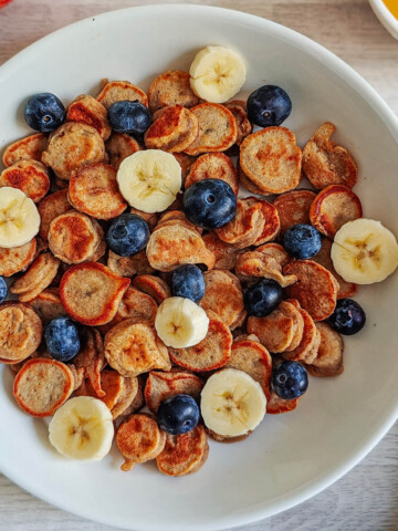 Des mini pancakes banane moelleux, dans une assiette avec des fruits.