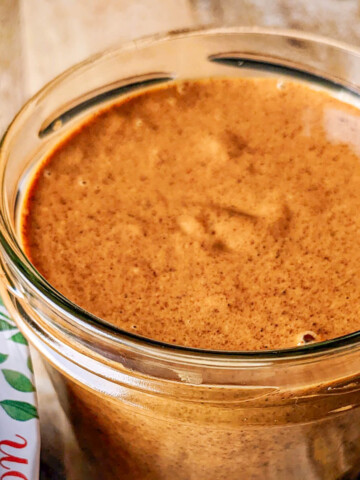 Pot en verre rempli de praliné amande maison onctueux avec un couvercle décoratif 'Fait Maison' posé à côté.