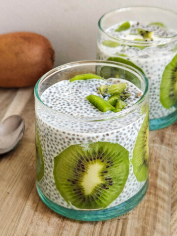Gros plan sur un pudding aux graines de chia onctueux dans un verre transparent, mettant en avant le dressage élégant avec des tranches de kiwi vert vif, ambiance petit-déjeuner sain et naturel.