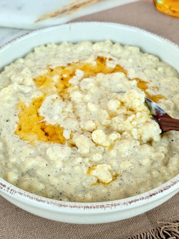 Bol de riz au lait vanille onctueux nappé d'un sirop doré, présenté sur une table en marbre avec une cuillère en bois.